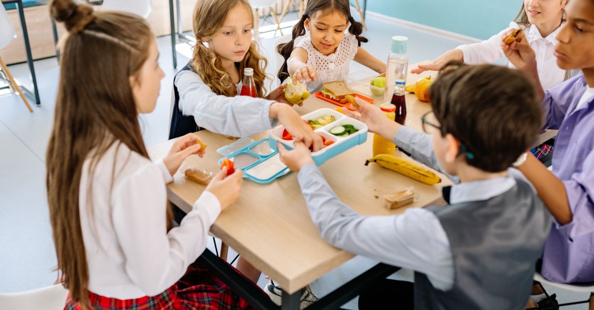 Group of diverse children having lunch in a school canteen, sharing and enjoying healthy snacks.